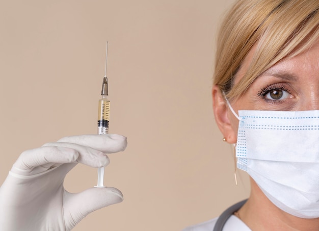 Medico donna con maschera medica che tiene la siringa del vaccino