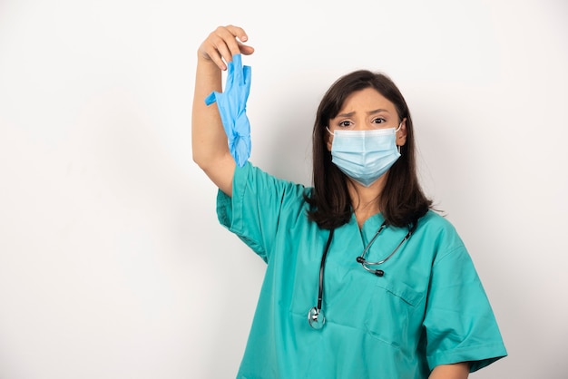 Medico donna con maschera tenendo i guanti su sfondo bianco. Foto di alta qualità