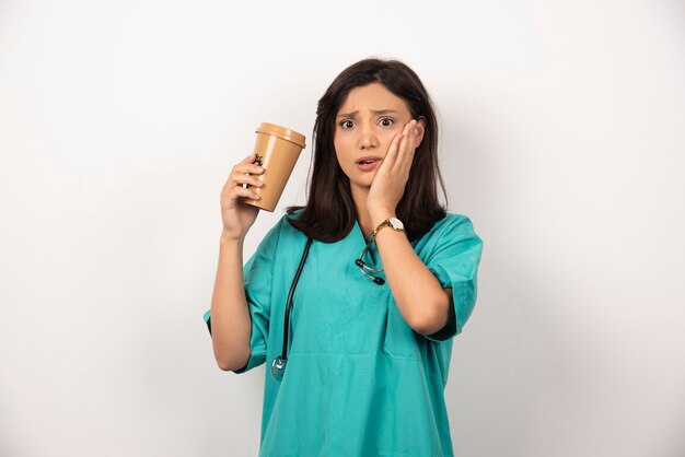 Medico donna con una tazza di caffè tenendo la sua guancia su sfondo bianco. Foto di alta qualità