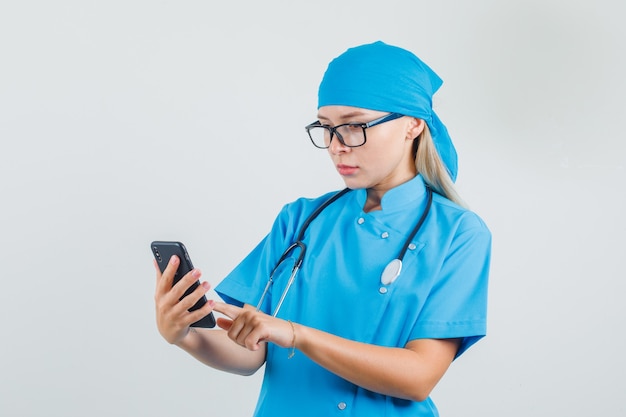 Medico donna utilizza lo smartphone in uniforme blu, occhiali e sembra occupato