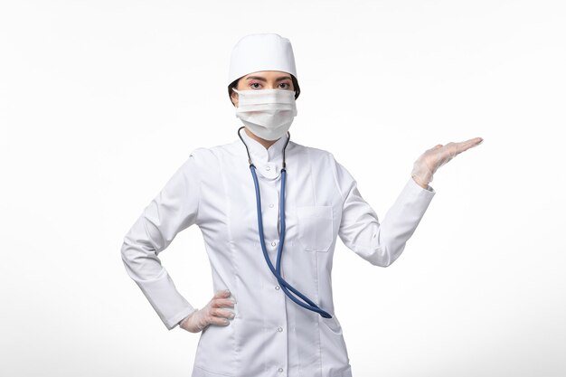 Medico donna vista frontale in tuta medica sterile bianca con maschera a causa di covid- sulla malattia da scrivania bianca covid- malattia pandemica
