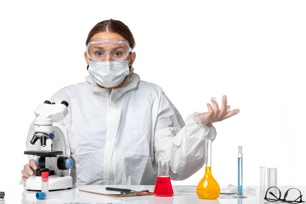 Medico donna vista frontale in tuta protettiva e con maschera utilizzando microscopio su sfondo bianco chiaro medicina covid- salute virus pandemico