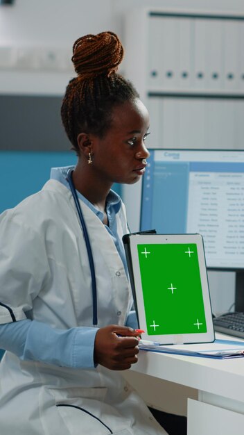 Medico e paziente afroamericani che esaminano lo schermo verde sul tablet per la visita di controllo. Medico nero che tiene verticalmente sfondo isolato e modello mockup con chiave cromatica sul display