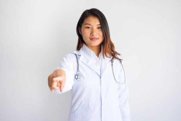 Medico femminile asiatico sorridente che indica voi.