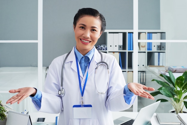 Medico femminile asiatico sorridente che posa nell'ufficio