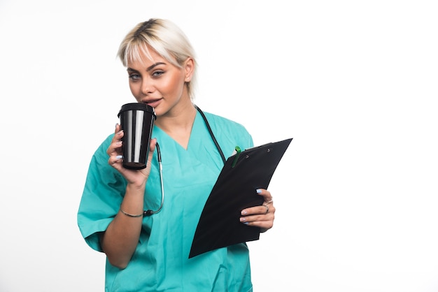 Medico femminile che beve tazza di caffè sulla parete bianca.