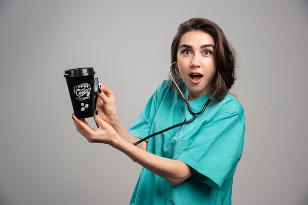 Medico femminile che controlla la tazza di caffè con lo stetoscopio. Foto di alta qualità