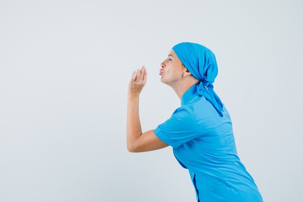 Medico femminile che fa il gesto gustoso con le labbra imbronciate in uniforme blu e sembra felice. .