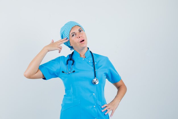 Medico femminile che imita il gesto di suicidio in uniforme blu e che sembra fiducioso. vista frontale.