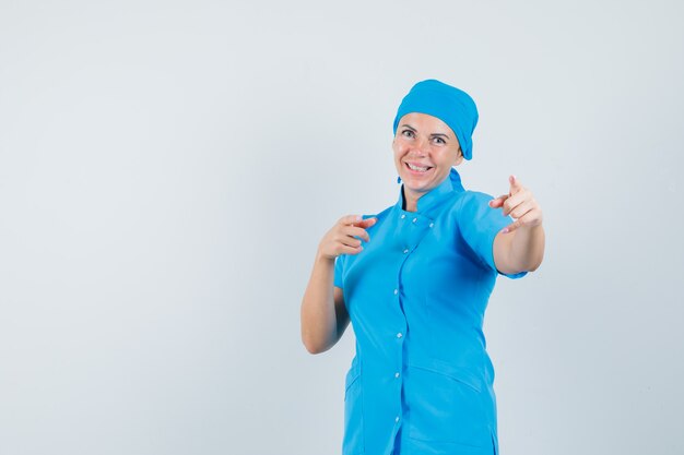Medico femminile che indica alla macchina fotografica in uniforme blu e che sembra allegro. vista frontale.