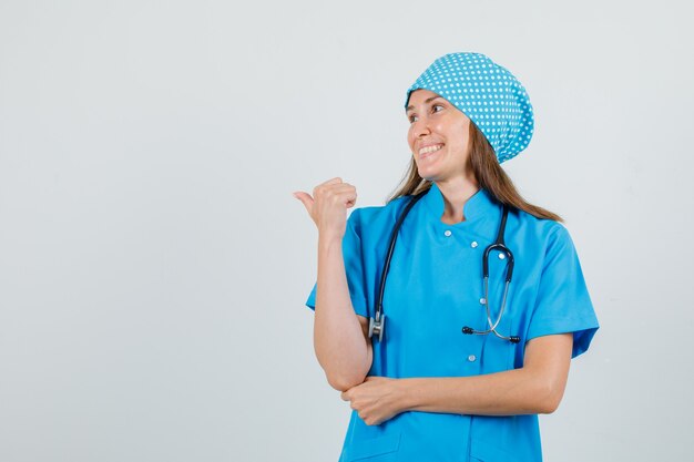 Medico femminile che indica il pollice indietro in uniforme blu e che sembra allegro