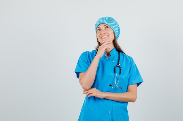 Medico femminile che mette la mano mentre si appoggia sul mento in uniforme blu e sembra allegro. vista frontale.