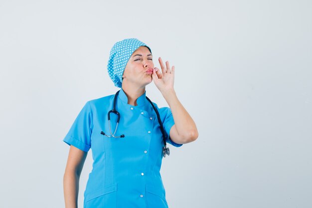 Medico femminile che mostra il gesto della chiusura lampo in uniforme blu e guardando attento, vista frontale.