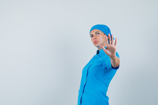 Medico femminile che mostra il gesto di arresto in uniforme blu e guardando ansioso, vista frontale.