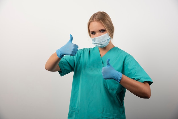 Medico femminile che mostra pollice in su e indossa una maschera medica.