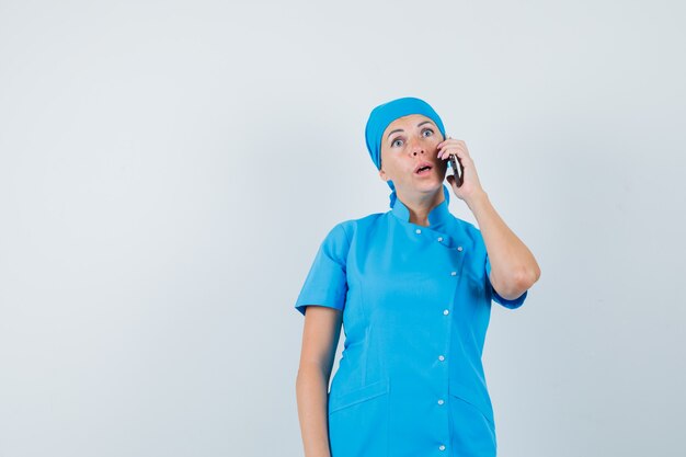 Medico femminile che parla sul telefono cellulare in uniforme blu e che sembra sorpreso. vista frontale.