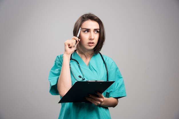 Medico femminile che pensa ai pazienti su sfondo grigio. Foto di alta qualità