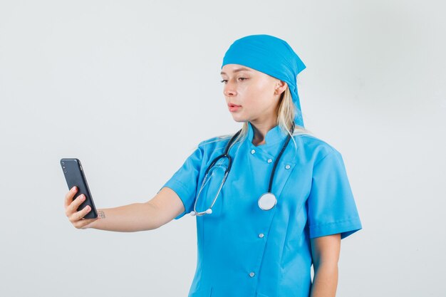 Medico femminile che tiene e che esamina smartphone in uniforme blu