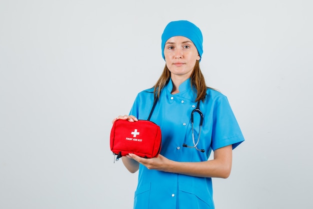 Medico femminile che tiene kit di pronto soccorso in uniforme e guardando attento