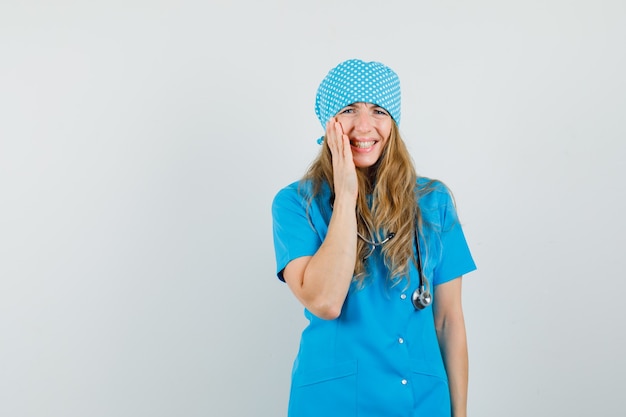 Medico femminile che tiene la mano sulla sua guancia in uniforme blu e che sembra depresso.