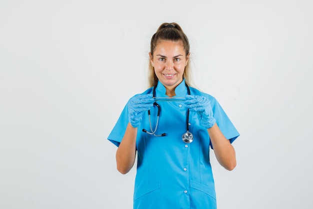 Medico femminile che tiene la provetta in uniforme blu, guanti e allegro