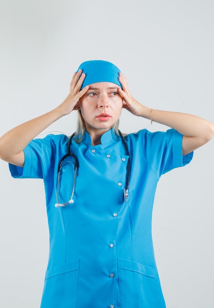 Medico femminile che tiene le mani alla testa in uniforme blu e che sembra infastidito