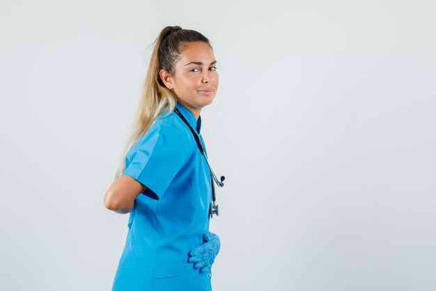 Medico femminile che tiene le mani sullo stomaco e sulla schiena in uniforme blu