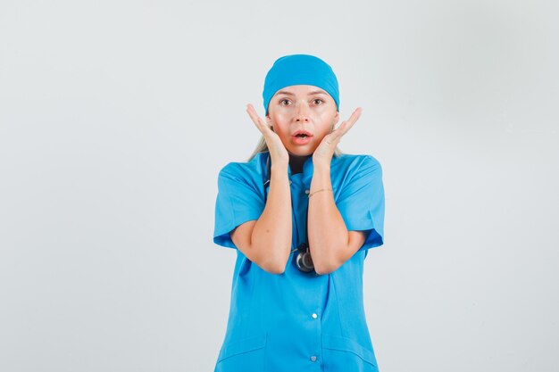 Medico femminile che tiene le mani vicino al viso in uniforme blu e che sembra spaventato