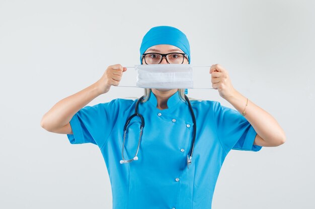 Medico femminile che tiene mascherina medica sopra la bocca in uniforme blu