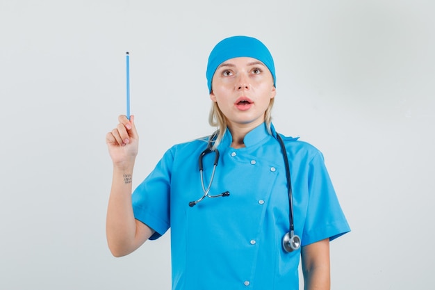 Medico femminile che tiene matita e che osserva in su in uniforme blu e che sembra premuroso