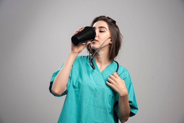 Medico femminile con la tazza di caffè bevente dello stetoscopio. Foto di alta qualità