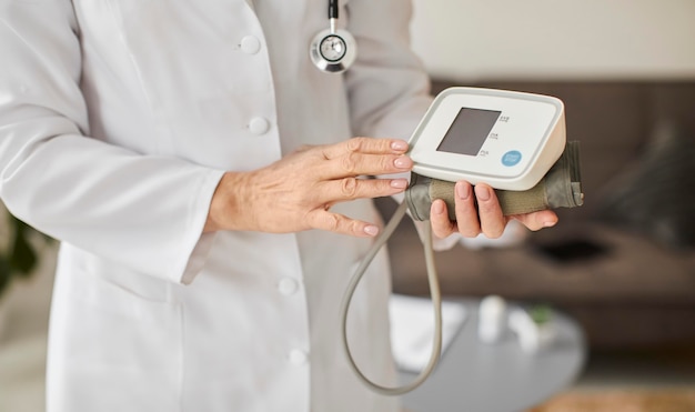 Medico femminile del centro di recupero covid anziano che tiene il monitor della pressione sanguigna