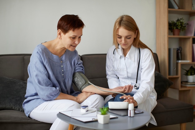 Medico femminile del centro di recupero Covid che controlla la pressione sanguigna del paziente anziano