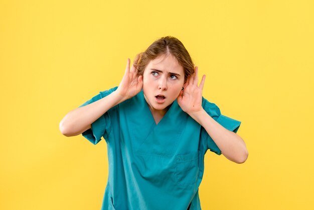 Medico femminile di vista frontale che ascolta sul virus dell'ospedale di salute del medico del fondo giallo