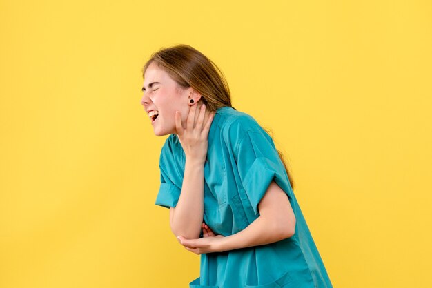 Medico femminile di vista frontale che ha mal di gola sull'emozione dell'ospedale del medico di salute del fondo giallo