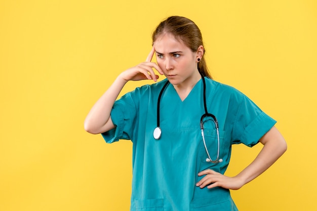 Medico femminile di vista frontale che pensa su un'emozione di salute dell'ospedale del medico del fondo giallo