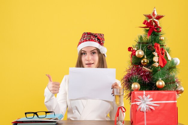 Medico femminile di vista frontale che si siede con i regali di natale che tengono i documenti su fondo giallo