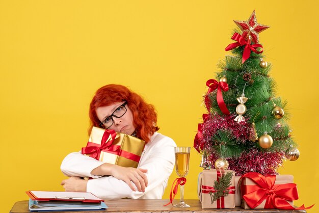 Medico femminile di vista frontale che si siede con i regali di Natale su priorità bassa gialla
