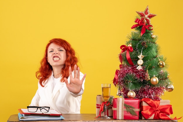 Medico femminile di vista frontale che si siede dietro la tavola con i regali di Natale sullo scrittorio giallo