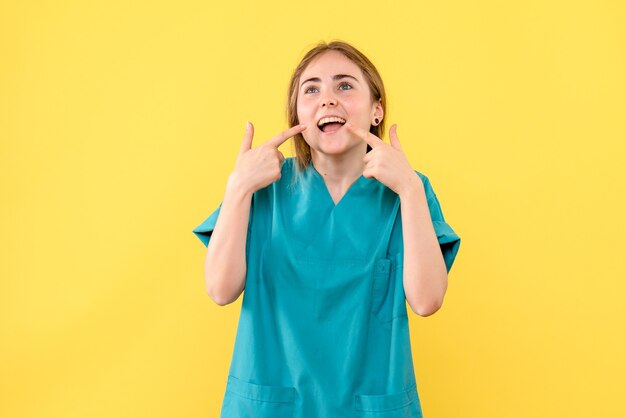 Medico femminile di vista frontale che sorride sulla salute dell'ospedale di emozione medica del fondo giallo