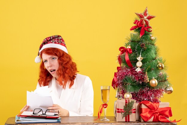 Medico femminile di vista frontale che tiene i documenti e seduto con i regali di Natale