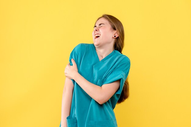 Medico femminile di vista frontale con dolore al braccio su sfondo giallo emozione ospedale medico sanitario