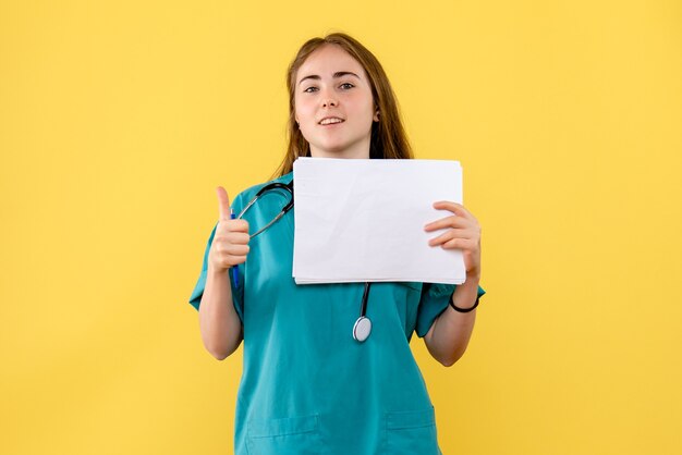 Medico femminile di vista frontale con la documentazione su una salute dell'ospedale dell'infermiera del fondo giallo