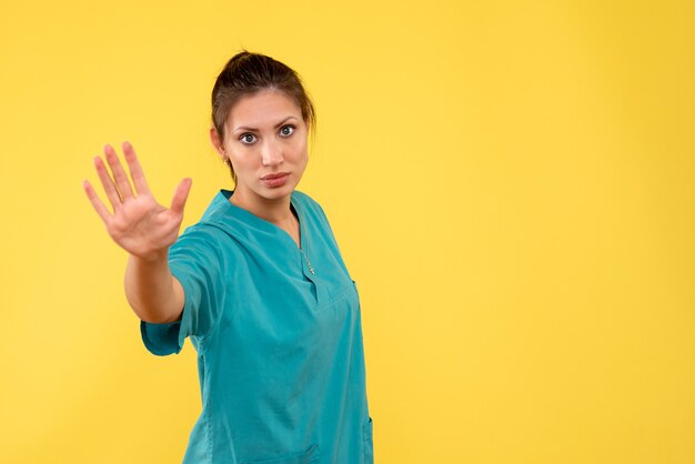 Medico femminile di vista frontale in camicia medica che chiede di fermarsi sullo sfondo giallo