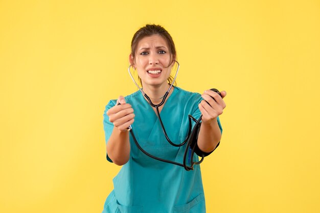 Medico femminile di vista frontale in camicia medica che controlla la sua pressione su priorità bassa gialla
