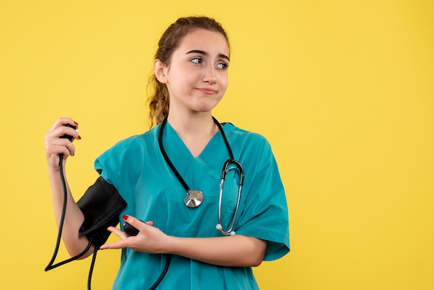 Medico femminile di vista frontale in camicia medica che controlla la sua pressione, uniforme pandemica covid-19 di emozione di salute del virus