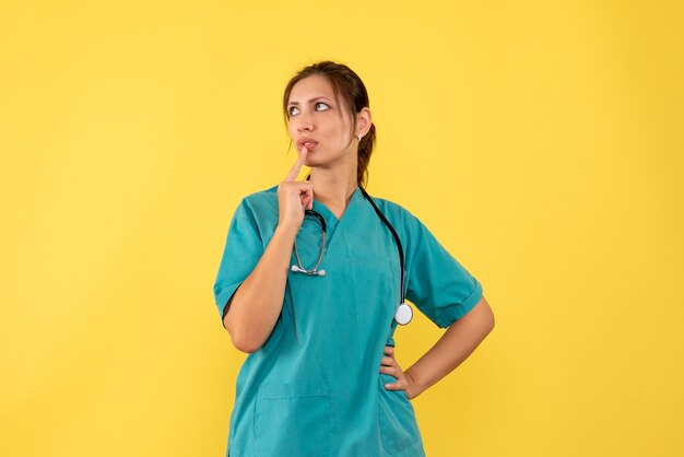 Medico femminile di vista frontale in camicia medica che pensa su fondo giallo
