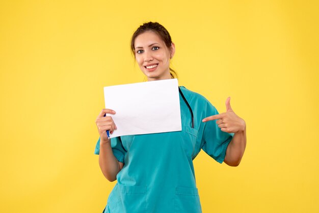 Medico femminile di vista frontale in camicia medica che tiene analisi della carta su fondo giallo