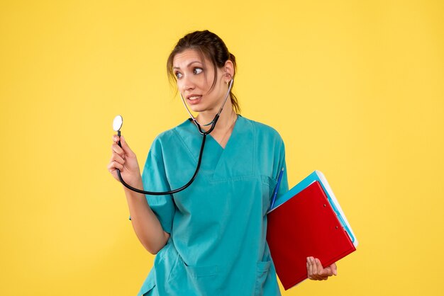 Medico femminile di vista frontale in camicia medica con lo stetoscopio e le note su fondo giallo