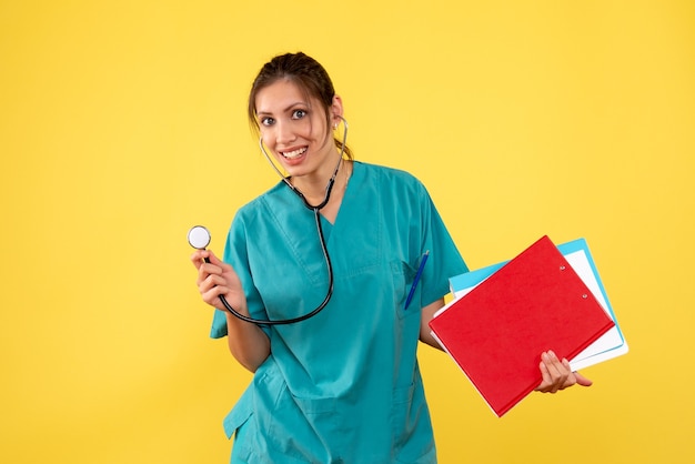 Medico femminile di vista frontale in camicia medica con lo stetoscopio e le note su fondo giallo